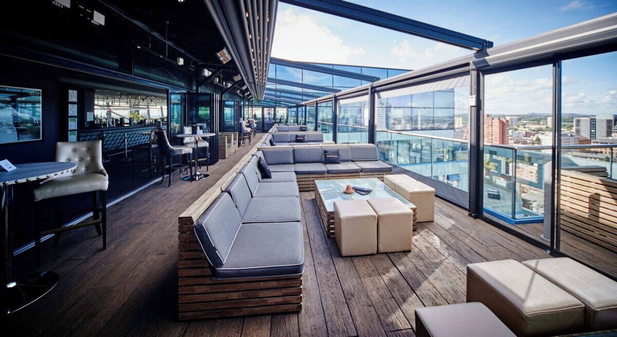 Un salon sur le toit, doté d’un espace salon, d’un bar et de grandes fenêtres offrant une vue sur la ville.