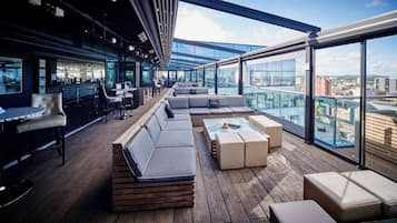 Eine Dachterrasse mit Sitzgelegenheiten, einer Bar und großen Fenstern mit Blick auf die Stadt.