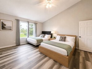 A bedroom with two beds, a ceiling fan, a window with curtains, and a door. - Insurance & Workers | 5 Beds | Easy S (Grayslake)