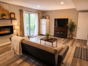 A living room with a sofa, a coffee table, a television, a fireplace, and a sliding glass door leading to a balcony.