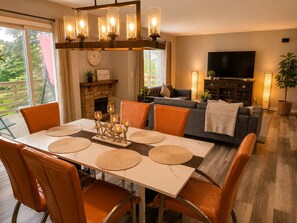 A dining area with a table set for four, surrounded by chairs, a fireplace, and a television in the background. - Insurance & Workers | 5 Beds | Easy S (Grayslake)