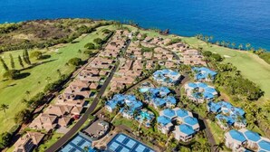 Vista aérea de un complejo turístico costero con varias construcciones, un campo de golf y una vista despejada del océano.