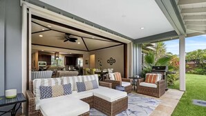 Un patio abierto con mobiliario de mimbre, una parrilla y vista al jardín trasero.