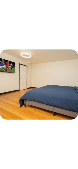 Een slaapkamer met een bed, houten vloeren, een deur en een aan de muur bevestigde televisie.