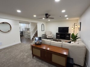 A living room with a sofa, a coffee table, a TV, and a ceiling fan. - Cozy 2BR Apartment Near Red Rocks & Mountains (Lakewood)