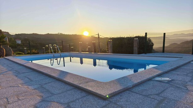 Ein rechteckiger Pool mit gefliestem Deck, umgeben von einem Zaun, mit freiem Blick auf den Sonnenuntergang im Hintergrund.