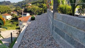Ein Kiesweg, eine Steinmauer und Blick auf eine Wohngegend mit Häusern und Grünflächen.