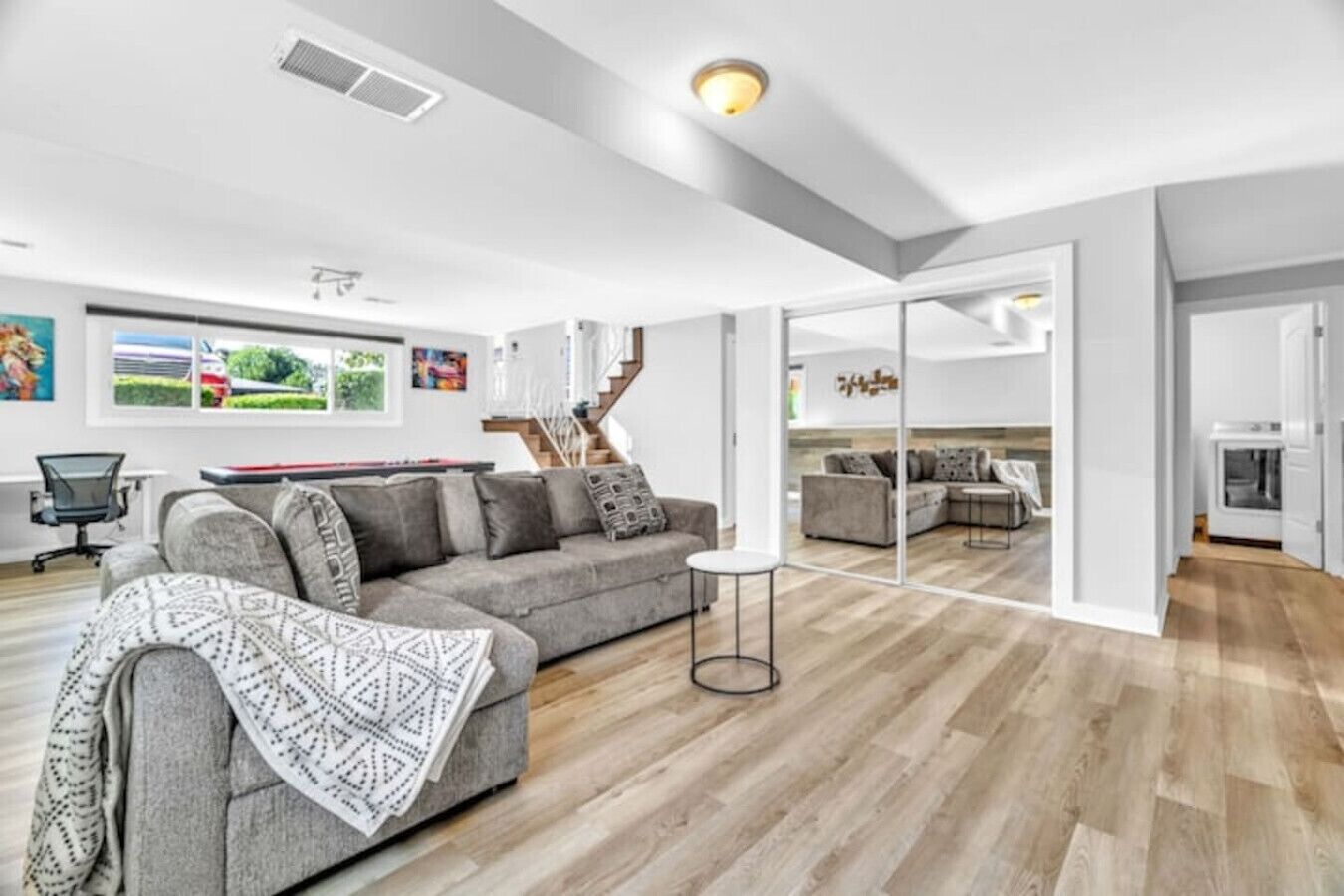 Un salon moderne avec un canapé gris, une petite table ronde et un escalier menant à un espace repas.