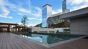 A modern hotel with a swimming pool, a covered outdoor area, and a view of a tall building in the background. - Acacia (San Pedro Garza García)