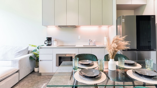 A modern kitchen with a dining table set for four, a coffee maker, and a refrigerator. - Acacia (San Pedro Garza García)