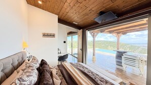 Ett modernt rum med en säng, ett skrivbord och utsikt över en pool och ett vackert landskap.