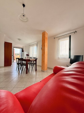 Un grand salon comprenant un coin repas avec une table, un canapé rouge et un téléviseur.