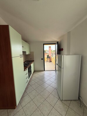 A kitchen with a stove, sink, and refrigerator. There is a door leading to an outdoor area with a view of buildings. - Sardinia Posada Paradise: Your home by the sea (Posada)