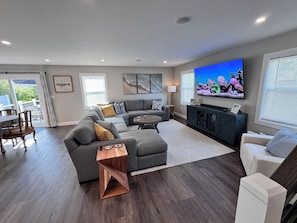 A modern living room with a sectional sofa, a flat-screen TV, and a dining area with a table and chairs.