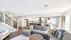 Ein modernes Wohnzimmer mit einem Ecksofa, einem runden Couchtisch und einer Treppe, die zu einer oberen Etage führt.
