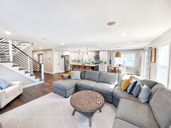 A modern living room with a sectional sofa, a round coffee table, and a staircase leading to an upper floor.