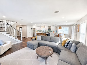 A modern living room with a sectional sofa, a round coffee table, and a staircase leading to an upper floor.