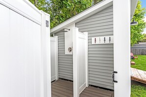 A covered outdoor area with a wooden deck, a white door, and a wall-mounted light fixture.