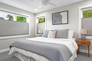 A bedroom with a bed, two bedside tables, a ceiling fan, and a window with blinds.