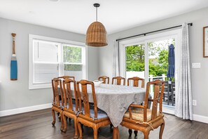 A dining area with a table set for six, surrounded by wooden chairs, a hanging light fixture, and a view through a glass door.