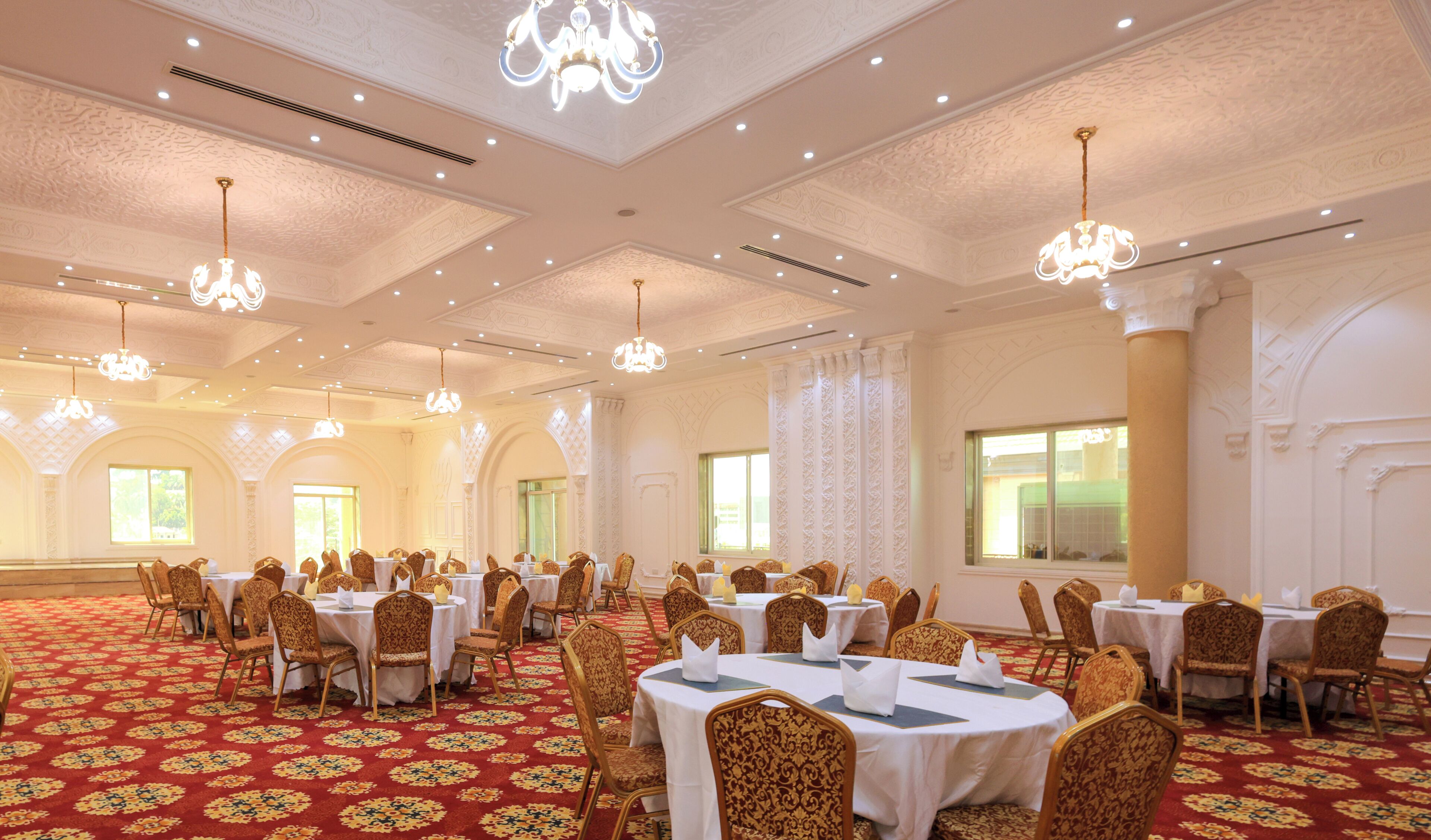 Un salón de banquetes con mesas redondas, sillas ornamentadas, candelabros y alfombra estampada.