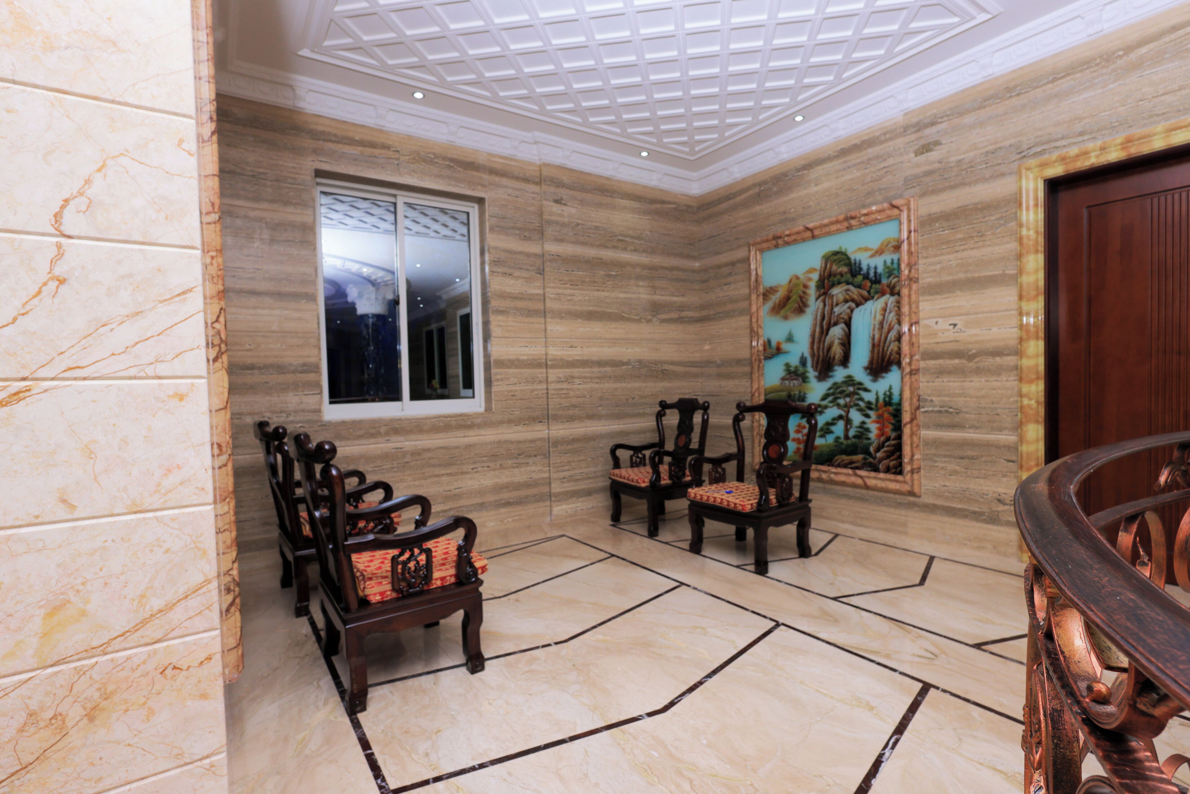 A room with a marble floor, wooden chairs, a painting, and a wooden door.