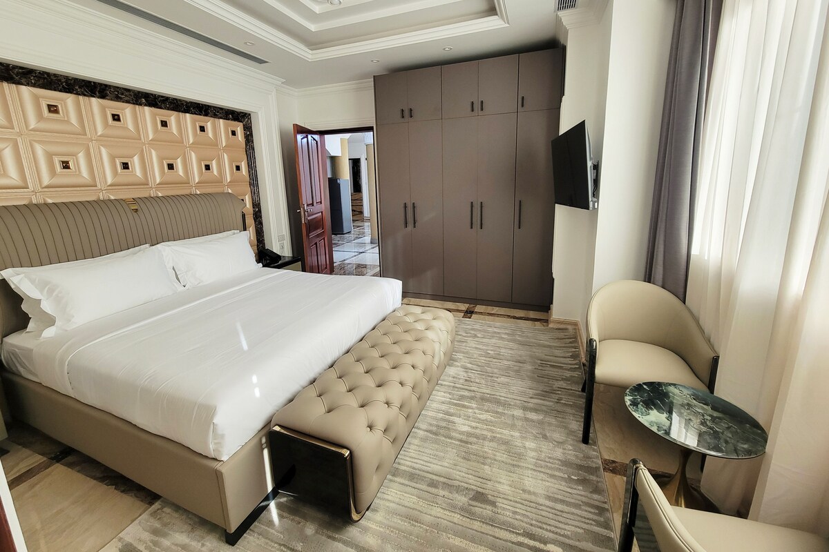 A hotel room with a large bed, a seating area, a wardrobe, and a television.