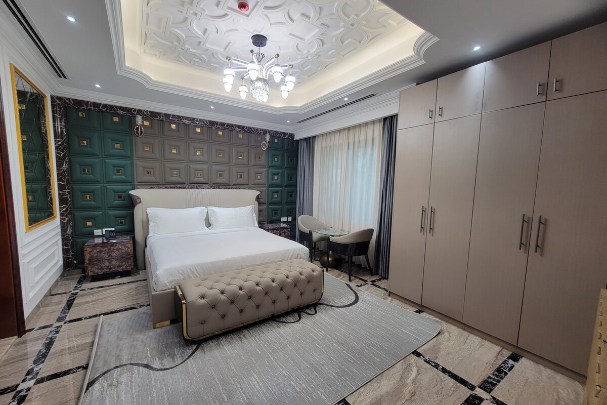 A bedroom with a large bed, a chest of drawers, a vanity, and a wardrobe.