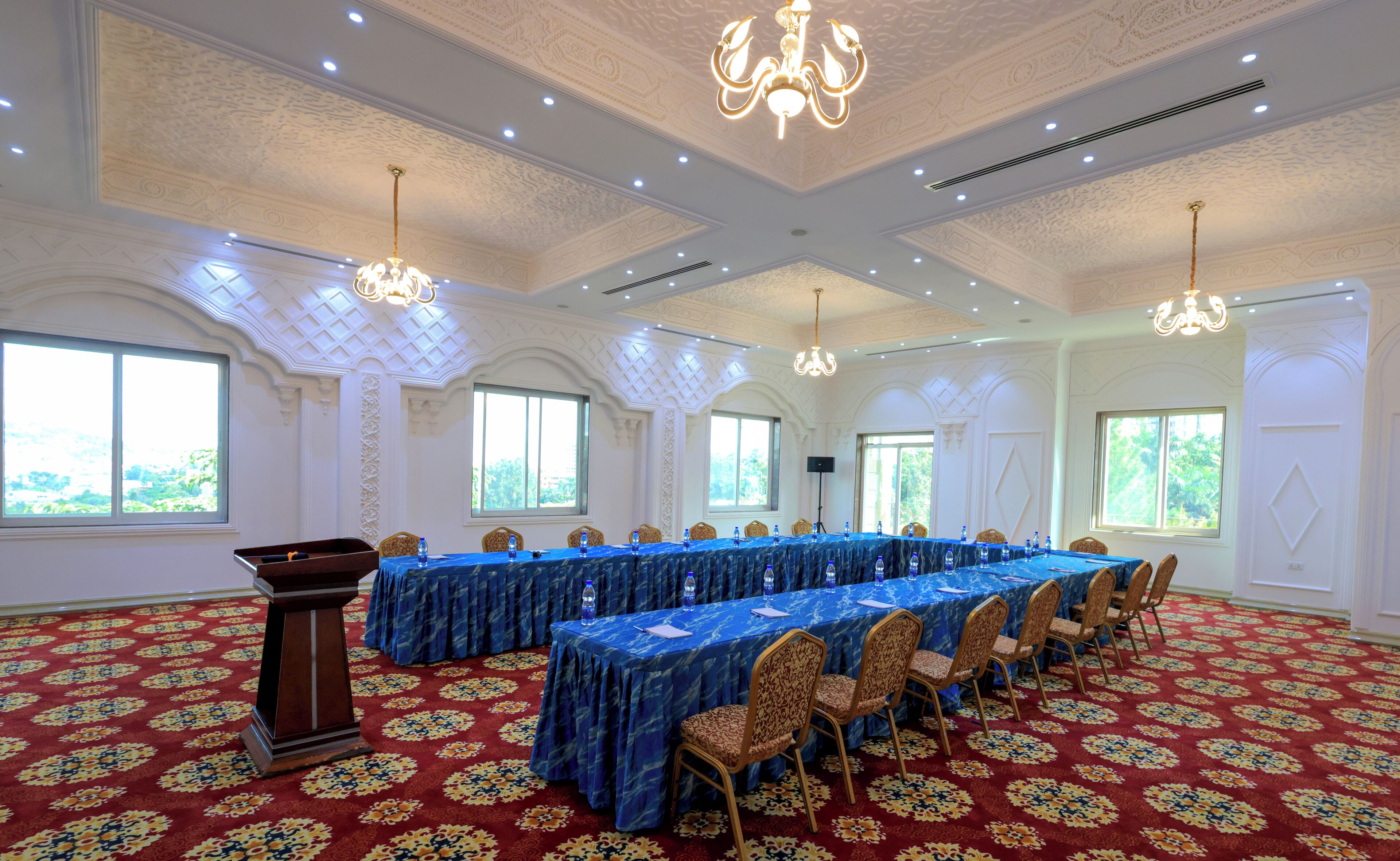 A conference room with a long table, chairs, a podium, and chandeliers.
