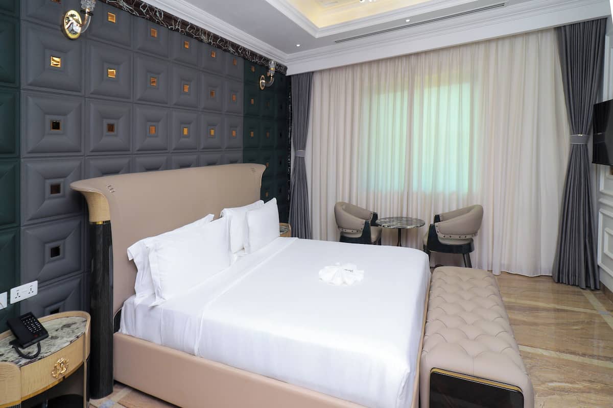 Una habitación de hotel con una cama grande, una mesita redonda pequeña, dos sillas, un banco, un televisor y una pared con un diseño geométrico.