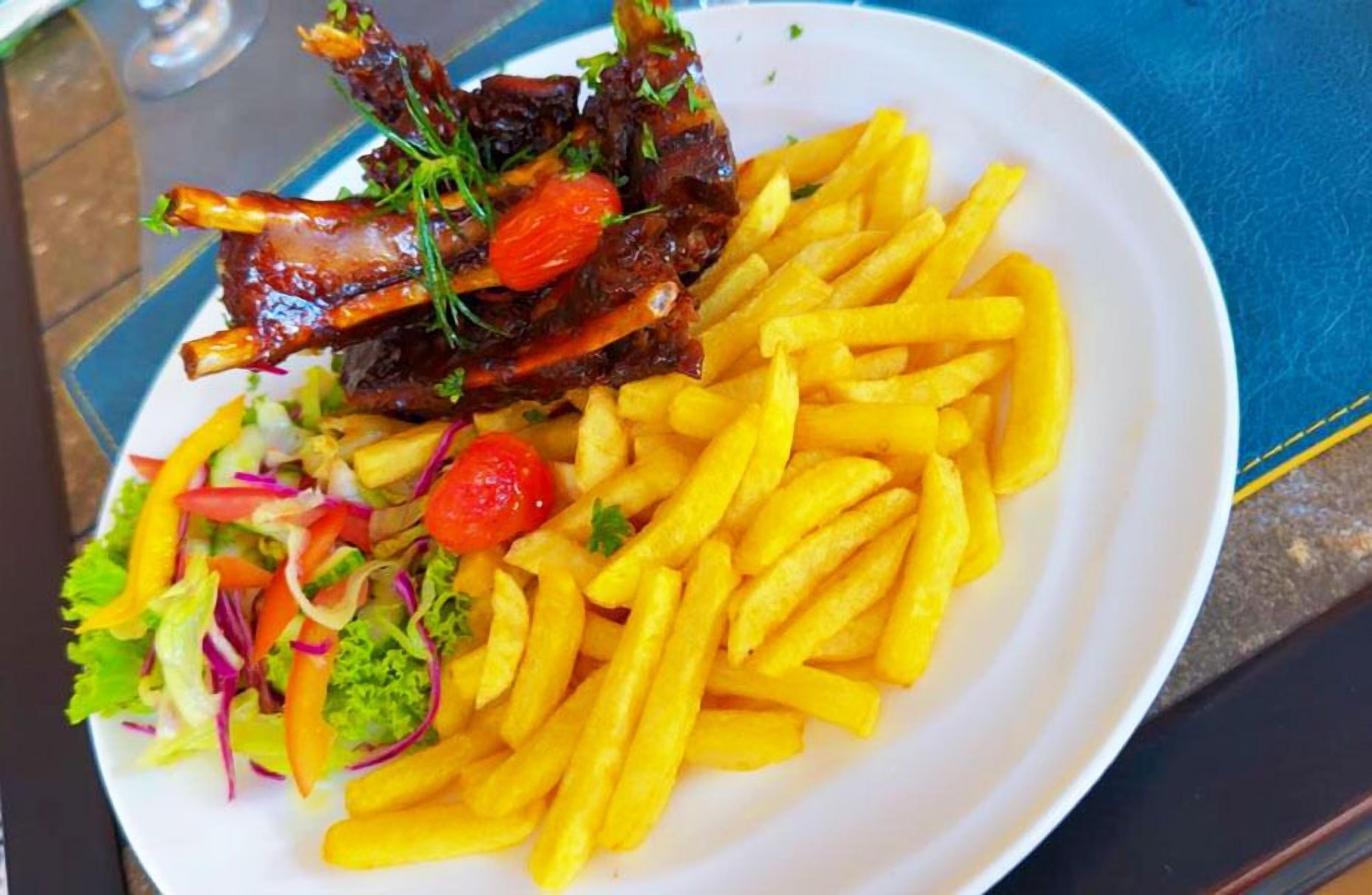 Um prato com um ensopado de carneiro, batatas fritas e uma salada de legumes.