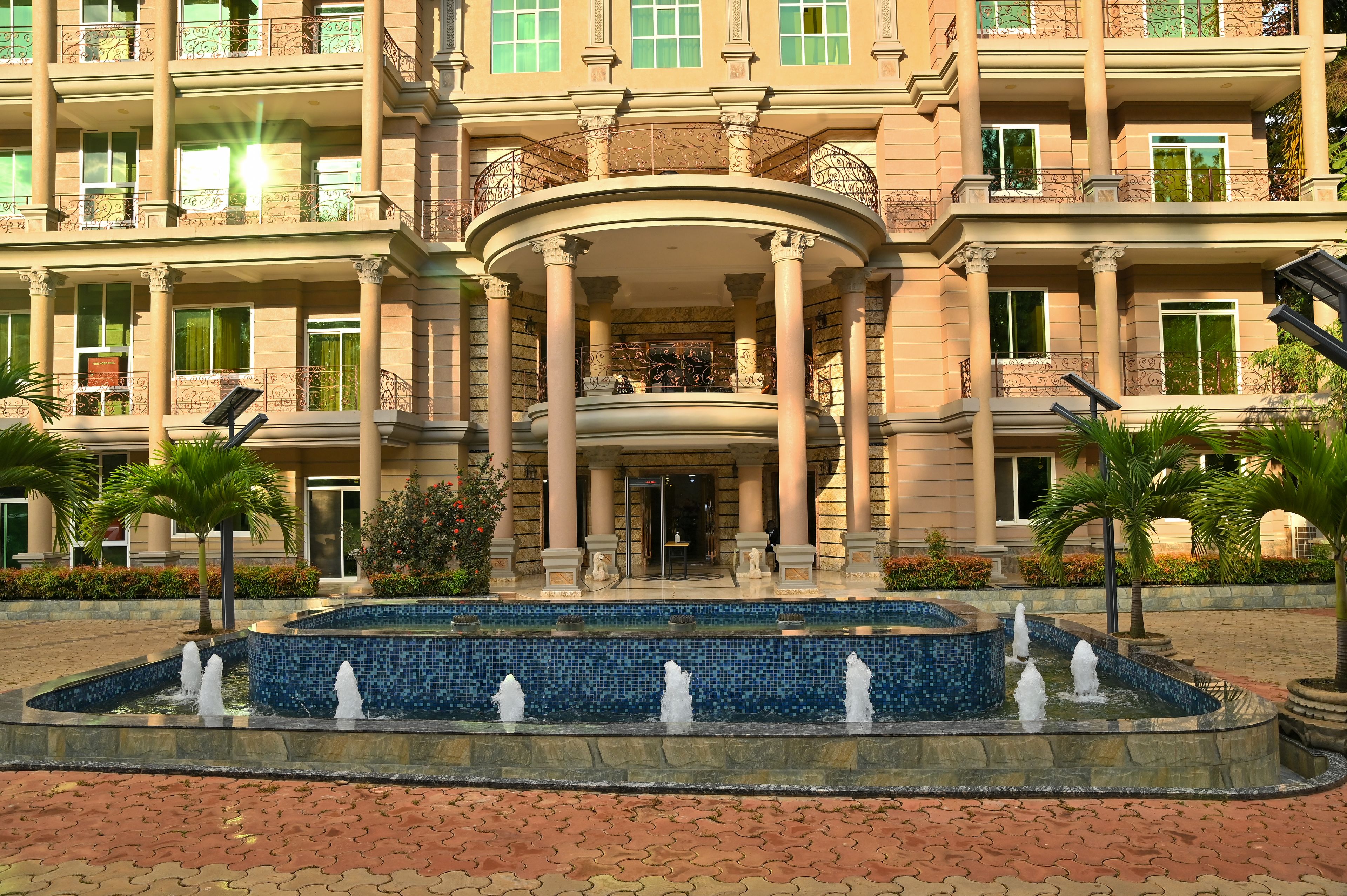A hotel entrance with a fountain, columns, and a well-maintained garden.
