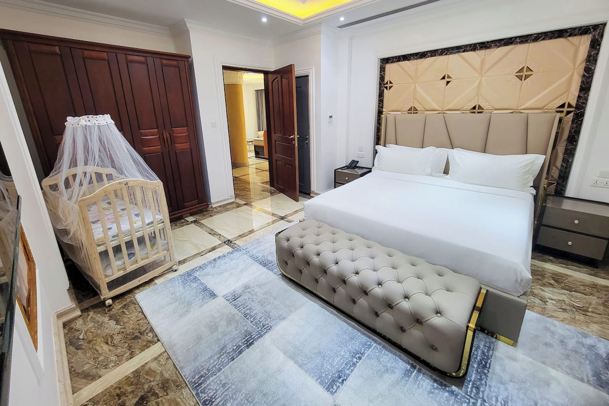 Un dormitorio con cama, mesitas de noche, armario y cuna con dosel.