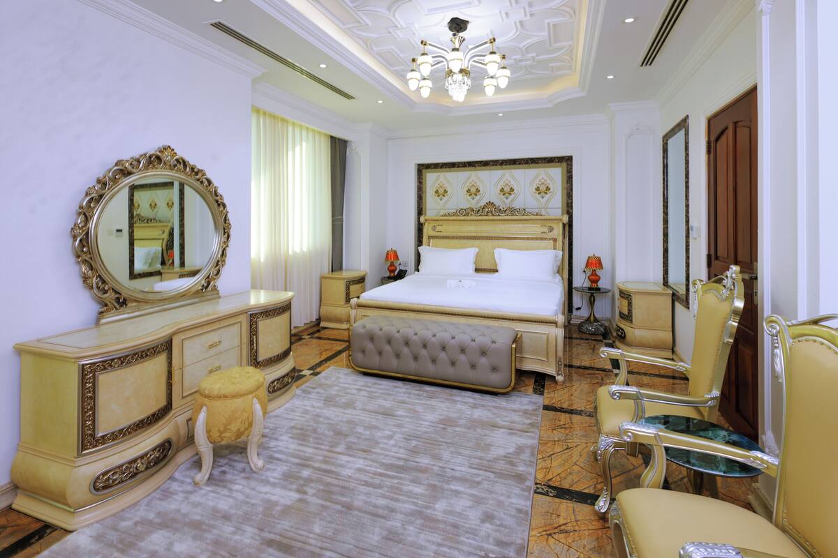 Un dormitorio lujoso con una cama grande, un tocador con espejo, un chaise lounge y una araña.