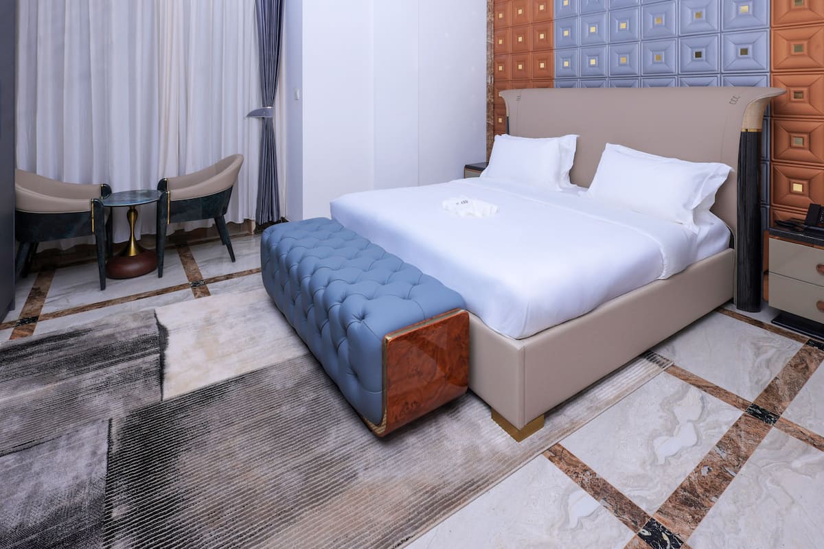Una habitación de hotel con una cama grande, una mesita pequeña y redonda, una silla y un cabecero decorativo.