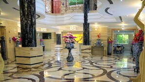 A lobby with marble flooring, a central floral arrangement, and a staircase leading to an upper level. - Fountain Palace Hotel & Suites (Kampala)