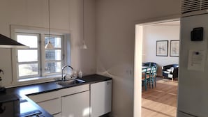 A modern kitchen with a sink, cabinets, and a window. There is a dining area with chairs and a table visible through an open door. - Holiday home with sea view in Sandkaas (Allinge-Sandvig)