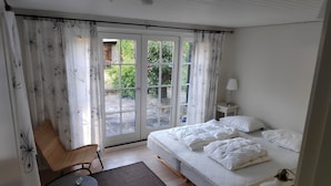 A bedroom with a bed, a chair, a table, a lamp, and a view through a door. - Holiday home with sea view in Sandkaas (Allinge-Sandvig)
