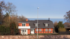 A two-story house with a stone wall, a red and white exterior, and a view of the sea. - Holiday home with sea view in Sandkaas (Allinge-Sandvig)