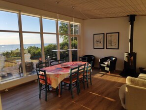 A dining area with a table, chairs, and a view through large windows. - Holiday home with sea view in Sandkaas (Allinge-Sandvig)