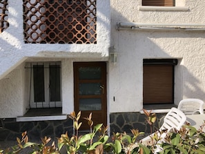A building with a white exterior, a wooden door, a window with a metal grill, a shuttered window, and a white chair outside. - Le cactus - STE-MARIE-LA-MER (STE-MARIE-LA-MER)