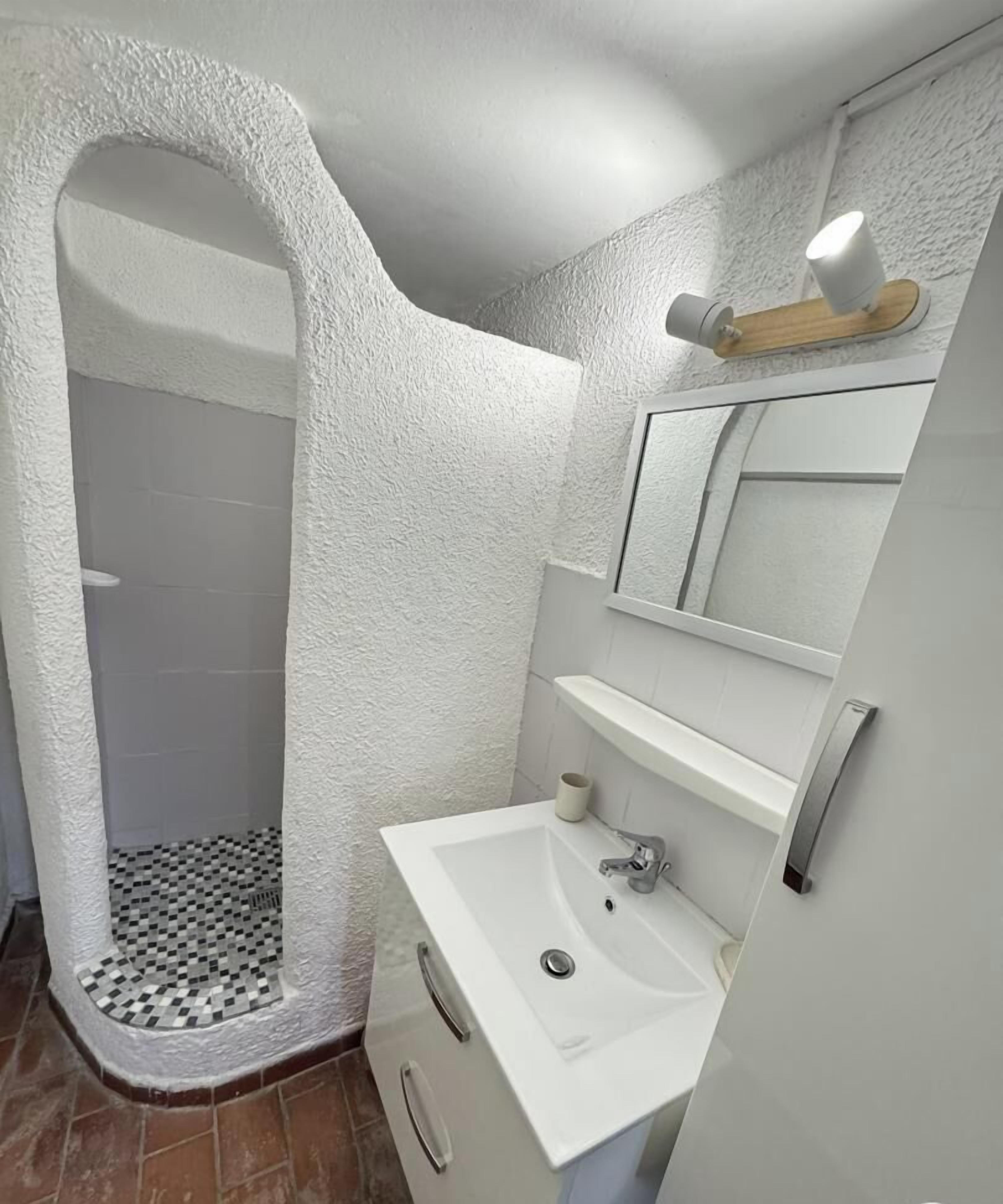 Een badkamer met een zwart-wit betegelde vloer, een witte wastafel, een spiegel en een douchehoek.