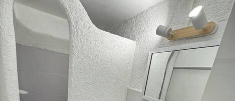 Een badkamer met een zwart-wit betegelde vloer, een witte wastafel, een spiegel en een douchehoek.