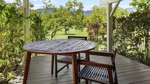 Un espacio al aire libre cubierto con una mesa y bancos, rodeado de abundante vegetación y vistas a un campo de golf.