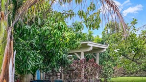 Un sendero en un jardín conduce a una estructura cubierta, rodeada de abundante vegetación y un césped cuidado.