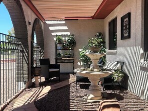 A covered patio with a stone wall, a metal gate, a chair, a table, a tiered planter, and a striped sofa. - The Gilbert Rustic Hideway (Gilbert)