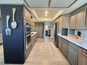 A modern kitchen with stainless steel appliances, a black brick accent wall, and a patterned rug. - The Gilbert Rustic Hideway (Gilbert)