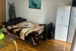 Um espaço de estar compacto com sofá, mesa de vidro, frigorífico e um quadro na parede.