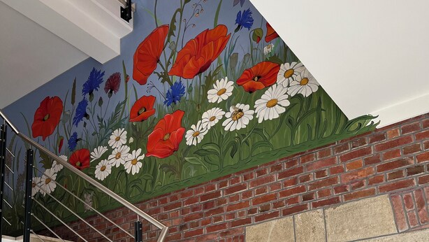 Eine Treppe mit Metallgeländer, einer Ziegelwand und einem Wandgemälde mit Blumen.