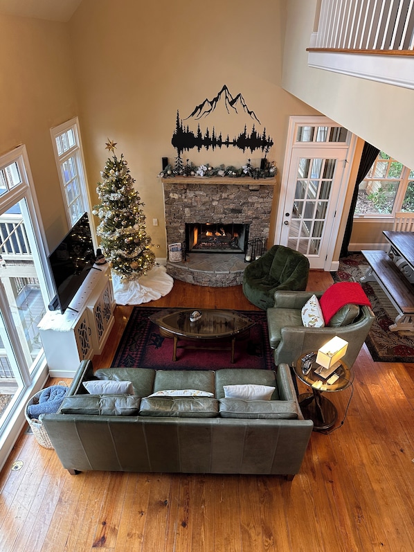 Una sala de estar acogedora con chimenea de piedra, un árbol de Navidad y un sofá verde.